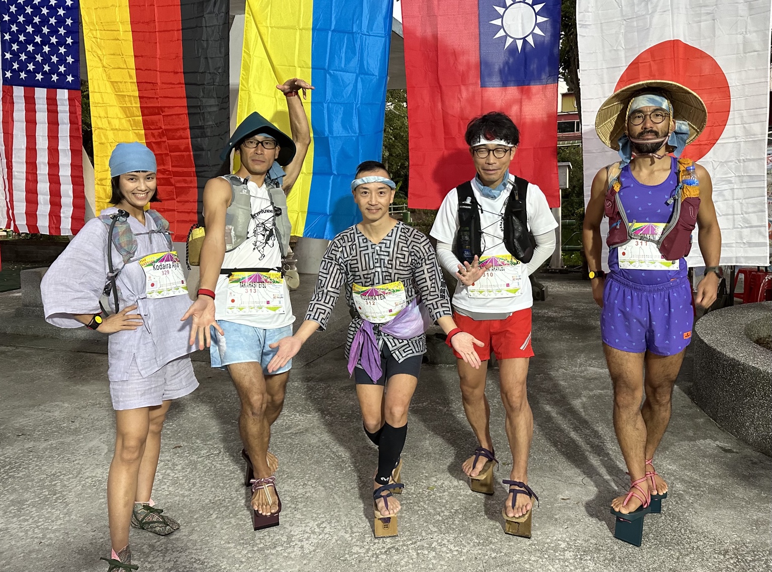 台湾のウルトラマラソン会場で各国の旗を背に並ぶTEN、綾理、モクエンら運営メンバー